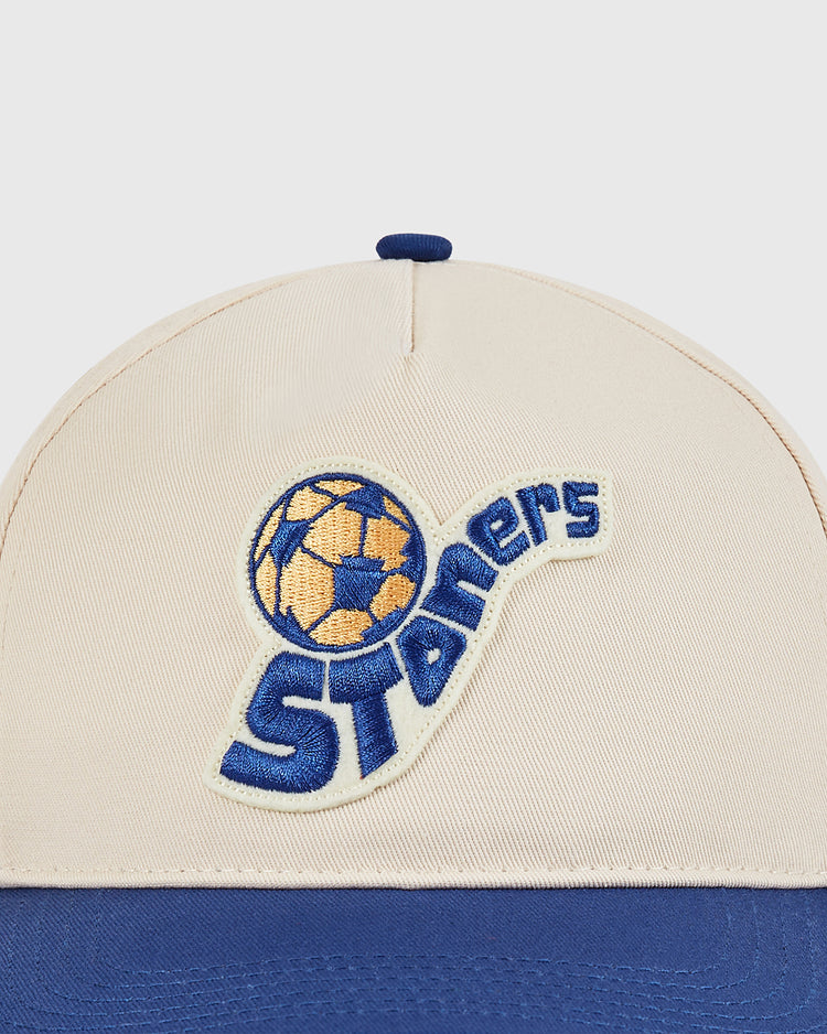 The Ebbets Field Pennsylvania Stoners A-Frame Cotton Twill Ballcap is beige and blue, featuring an embroidered yellow and blue soccer ball and bold blue “Stoners” text.