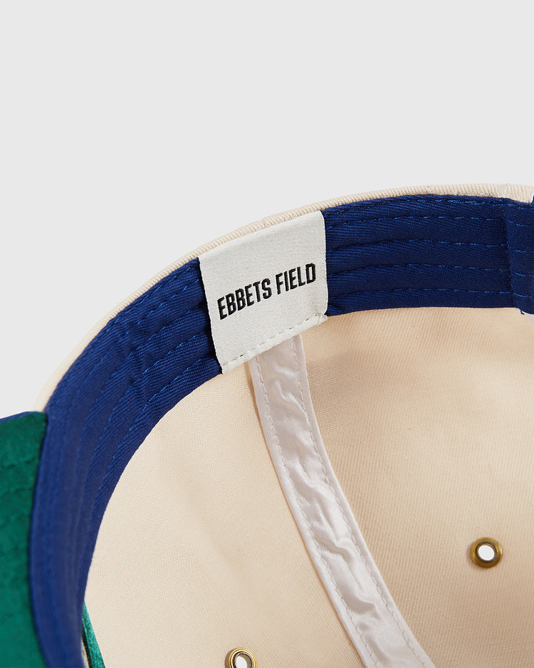 Close-up of the inside of the Pennsylvania Stoners A-Frame Cotton Twill Ballcap by Ebbets Field, showing a white label. The cap features blue, beige, and green fabric with gold ventilation eyelets visible.