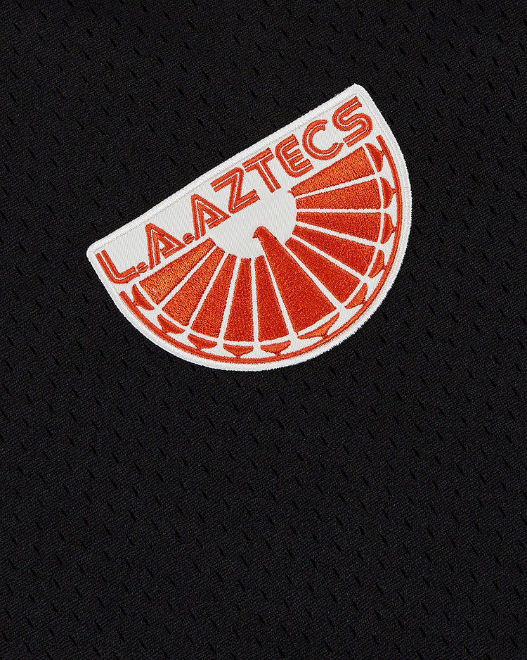 The Ebbets Field Los Angeles Aztecs Mesh Soccer Jersey is a black textured mesh jersey with a white and orange semicircle patch and bold orange L.A. AZTECS text, inspired by the iconic NASL team's classic look.