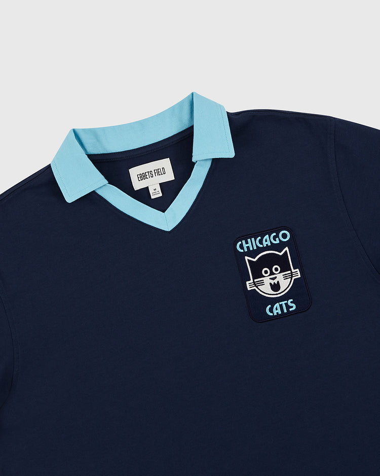 The Chicago Cats Vintage Collar Soccer Jersey by Ebbets Field features a navy cotton body, light blue collar, and chest patch with a cartoon cat’s face and CHICAGO CATS—an American Soccer League tribute. Inside label reads Ebbets Field.