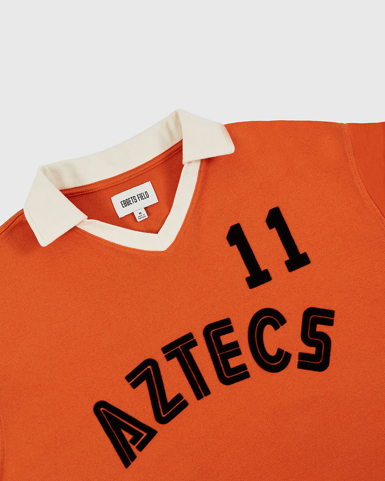 This Los Angeles Aztecs Vintage Soccer Goalie Jersey by Ebbets Field is an orange long sleeve shirt with a white collar, featuring the number 11 and bold AZTECS text—an eye-catching collector’s piece.