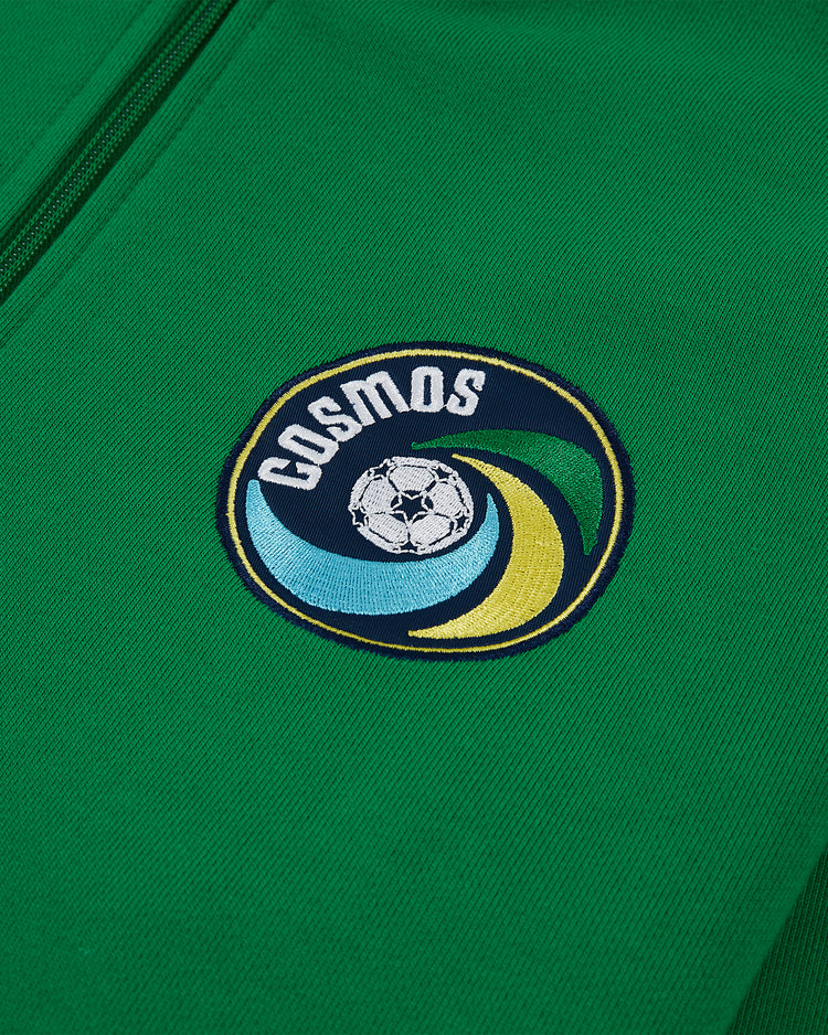 A close-up of the Ebbets Field New York Cosmos Soccer Warm Up Jacket, featuring a green zip design with an embroidered Cosmos logo—a stylized soccer ball with blue, yellow, and green accents inspired by Pelé and the legendary team.