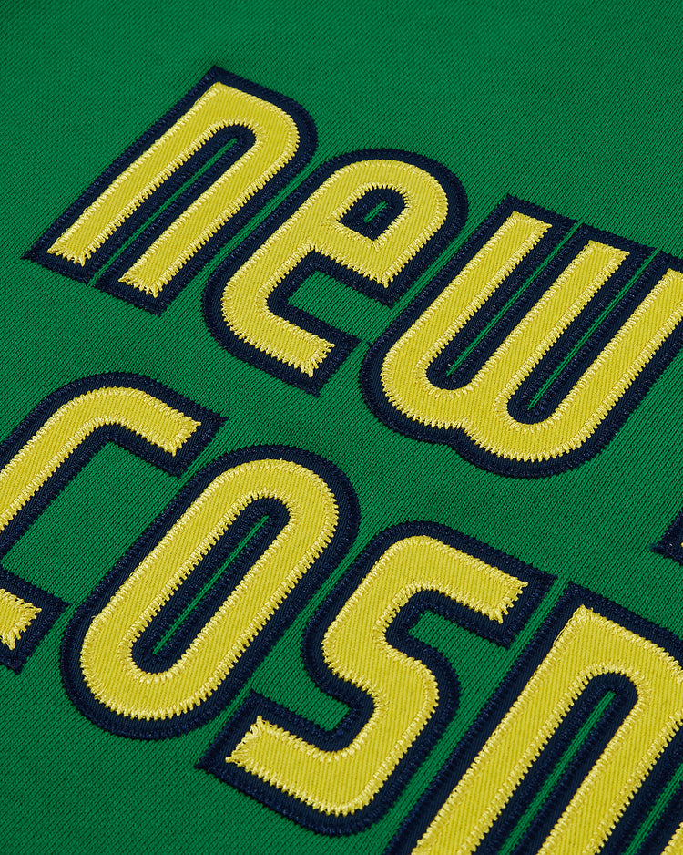 The Ebbets Field New York Cosmos Soccer Warm Up Jacket features green fabric with bold yellow letters outlined in dark blue, partially spelling out 