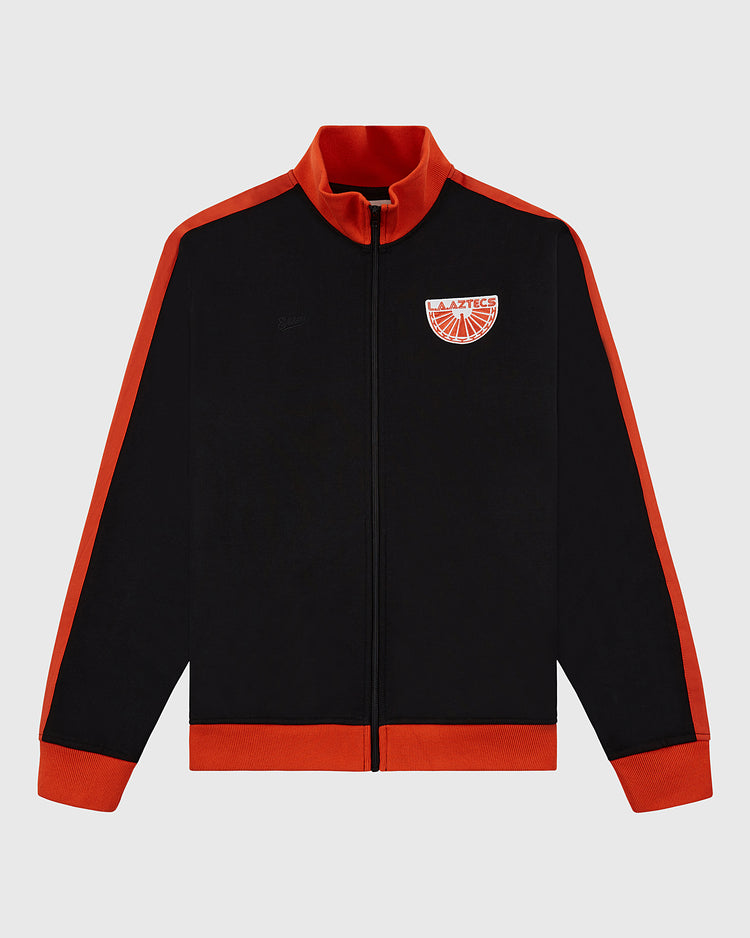 The Ebbets Field Los Angeles Aztecs Soccer Warm Up Jacket is black with red collar, cuffs, hem, and shoulder stripes. Features a NASL team emblem on the left chest, front zipper, and long sleeves for a sporty look.