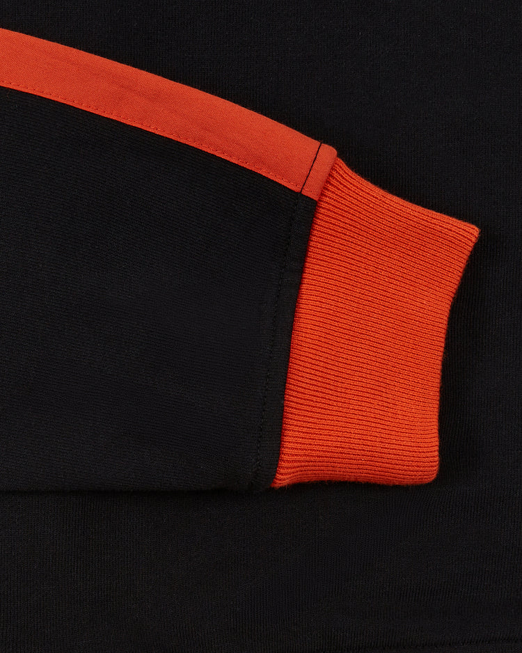 Close-up of the Ebbets Field Los Angeles Aztecs Soccer Warm Up Jacket, featuring black fabric, a red-orange cuff, and diagonal stripe details inspired by the NASL team. Textures and stitching are clearly shown.