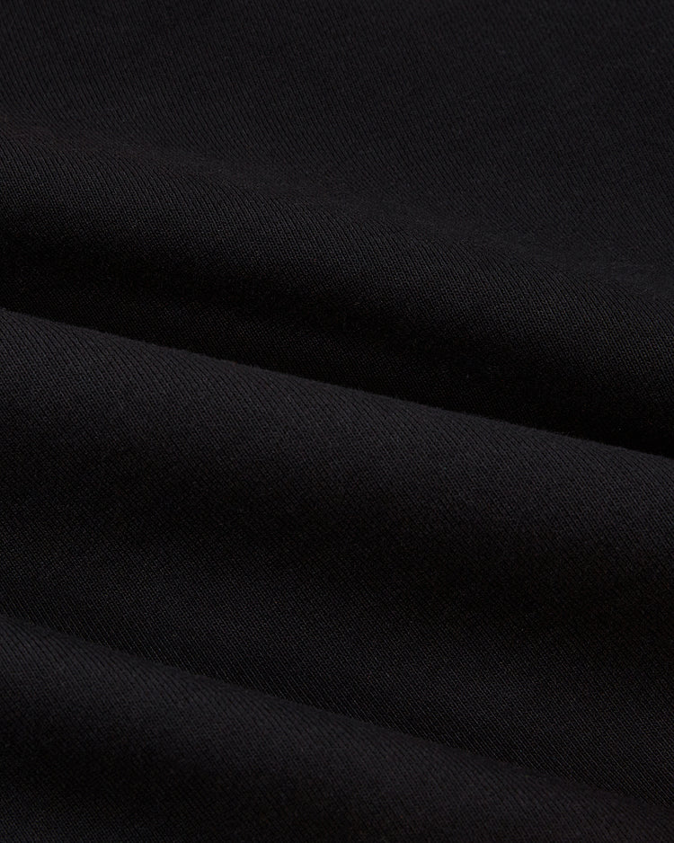 Close-up of black fabric from the Ebbets Field Los Angeles Aztecs Soccer Warm Up Jacket, showing its textured surface and soft diagonal folds that create subtle shadows and highlights on the material.