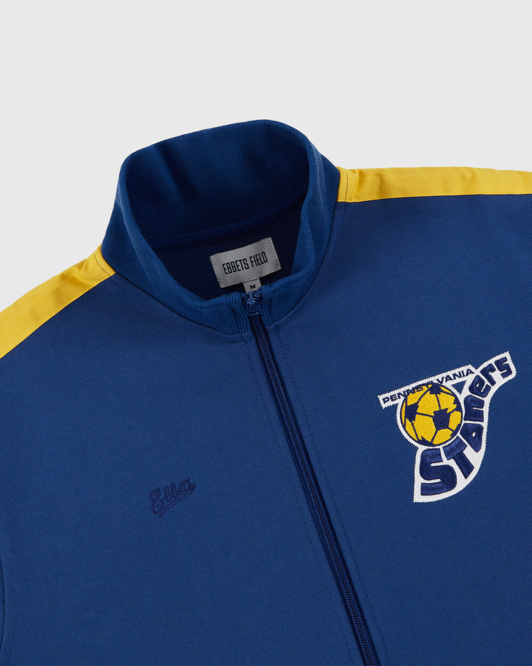 The Ebbets Field Pennsylvania Stoners Soccer Warm Up Jacket is blue with yellow shoulder stripes, a stitched Ella logo, and a team chest patch featuring a yellow soccer ball—honoring the ASL champions.
