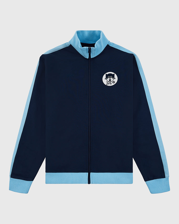 The Ebbets Field Chicago Cats Soccer Warm Up Jacket in navy features light blue cuffs, collar, and shoulder stripes, plus a left chest patch of a cartoon cat with glasses. The jacket is displayed flat on a white background.