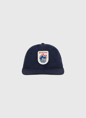The Ebbets Field Boston Minutemen Cotton Twill Ballcap is navy blue with a front patch showing a red and white shield, 