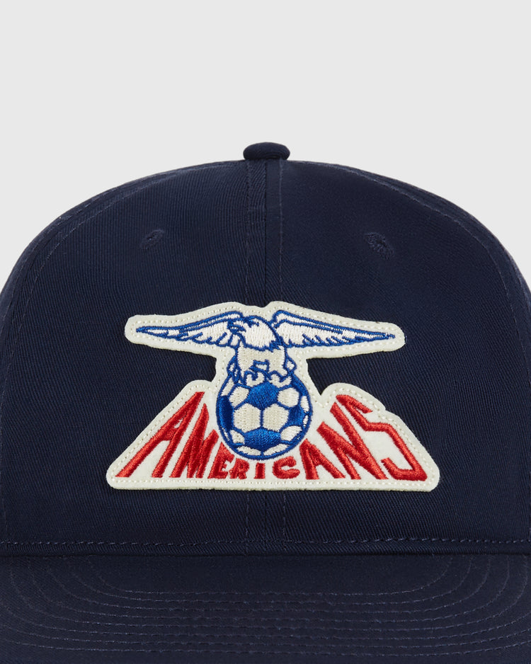The Ebbets Field New Jersey Americans Cotton Twill Ballcap features a navy blue design with an embroidered eagle holding a blue and white soccer ball above bold red 