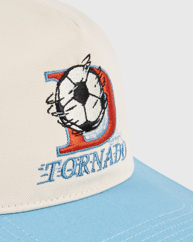 A close-up of the Dallas Tornados A-Frame Cotton Twill Ballcap by Ebbets Field shows beige and blue panels, embroidered TORNADO text, a stylized D with a spinning soccer ball, celebrating retro NASL style.