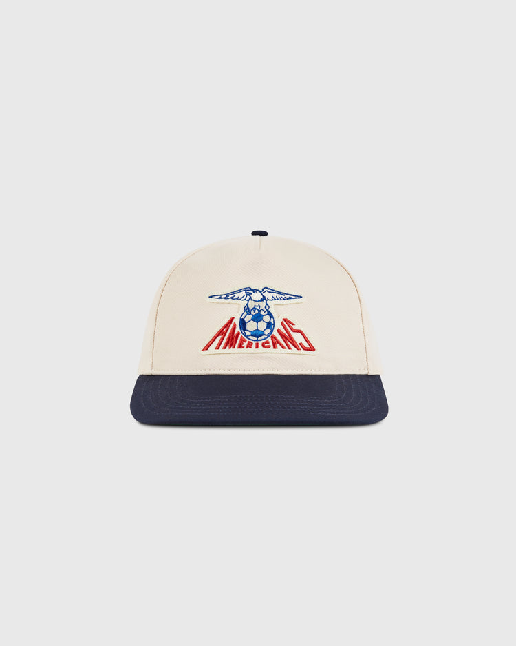 The Ebbets Field New Jersey Americans A-Frame Cotton Twill Ballcap features a beige crown, navy brim, blue eagle, and red AMERICANO text—a retro snapback inspired by the classic New Jersey Americans hat.