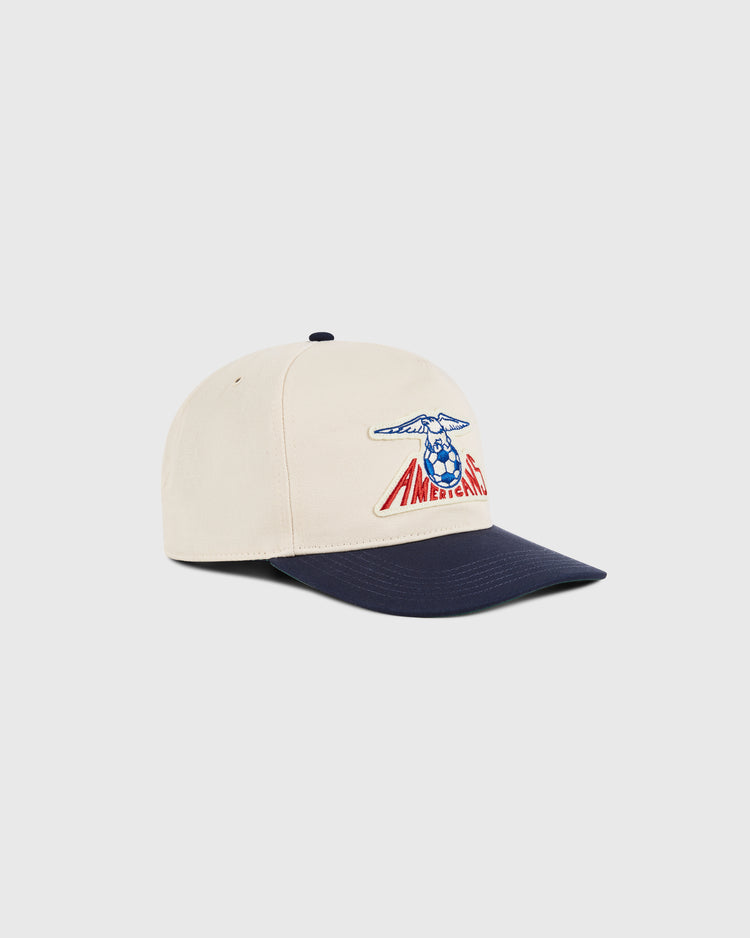 The Ebbets Field New Jersey Americans A-Frame Cotton Twill Ballcap features a beige retro look with a navy blue brim, embroidered blue and red Americana artwork, inspired by classic New Jersey Americans hat styles. Set on a plain white background.