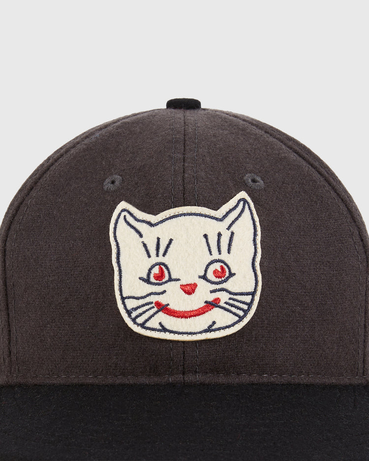 A close-up of the Ebbets Field Kansas City Katz 1961 Wool Ballcap featuring an embroidered white cat face with red eyes, nose, and smile on the front—a tribute to the vintage team.
