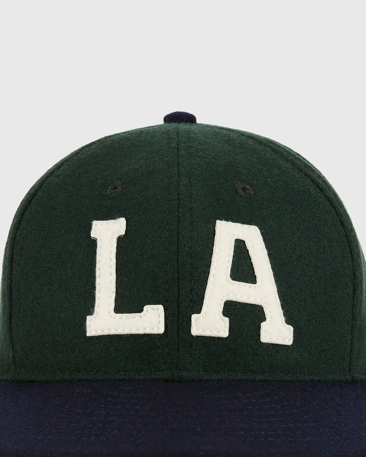 The Ebbets Field Los Angeles Angels (PCL) 1949 Wool Ballcap features a dark green crown, large white LA letters, Pacific Coast League inspiration, and a navy blue brim.