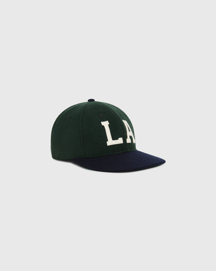 The Ebbets Field Los Angeles Angels (PCL) 1949 Wool Ballcap features dark green wool, a black brim, and bold white LA letters on the front, shown against a plain light gray background.