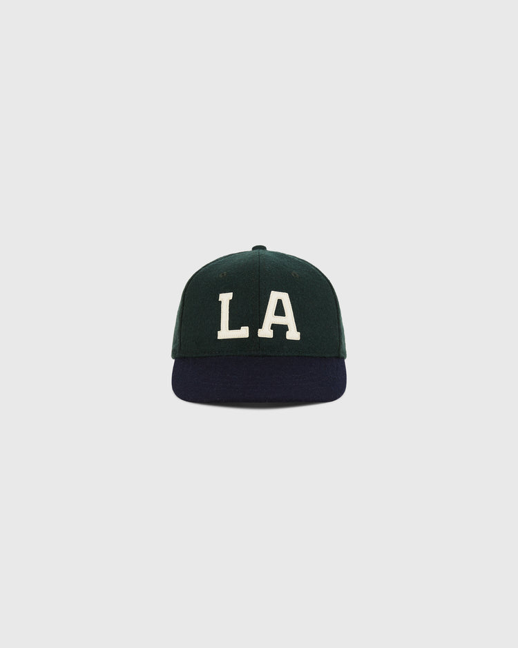 The Ebbets Field Los Angeles Angels (PCL) 1949 Wool Ballcap in youth size features a dark green crown, dark blue brim, and large white LA embroidery, shown against a light gray background.