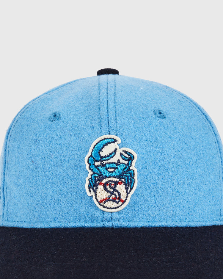 A close-up of the Ebbets Field Santurce Cangrejeros Crab Wool Ballcap for youth, featuring a blue crown, black brim, and an embroidered cartoon crab with a blue helmet on the front.
