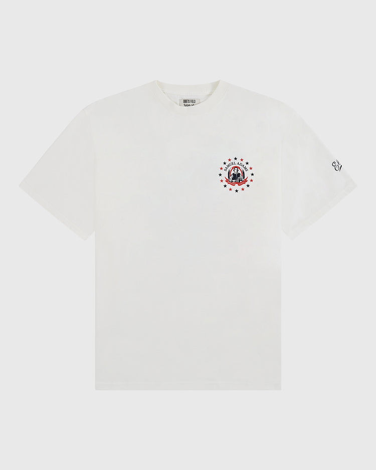 The Sam Adams Bottle Cap Short Sleeve Graphic T-Shirt by Ebbets Field features a small circular bottle cap graphic with stars and a face on the left chest and a subtle black logo on the left sleeve, celebrating our Ebbets Field collaboration.