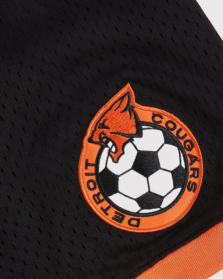 Close-up of the Detroit Cougars Mesh Soccer Jersey by Ebbets Field, featuring black mesh with an orange and white stitched cougar head and soccer ball patch, inspired by the original NASL Detroit Cougars kit.