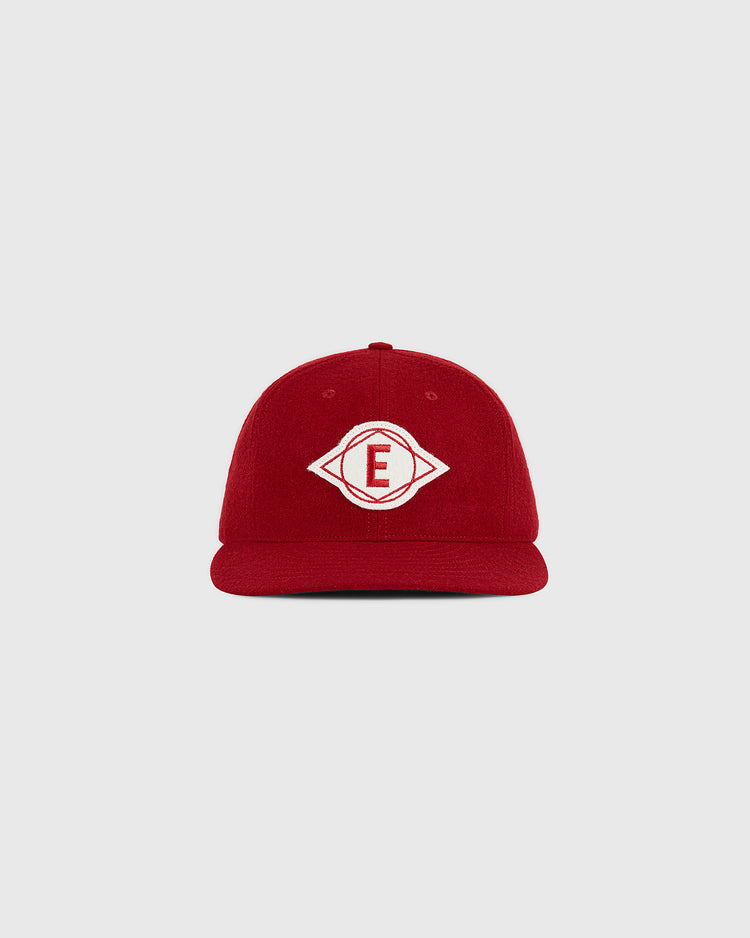 An Escogido Leones 1955 Authentic Wool Ballcap by Ebbets Field, in red wool with a white embroidered diamond-shaped logo featuring the letter “E” in the center, displayed on a plain light gray background.