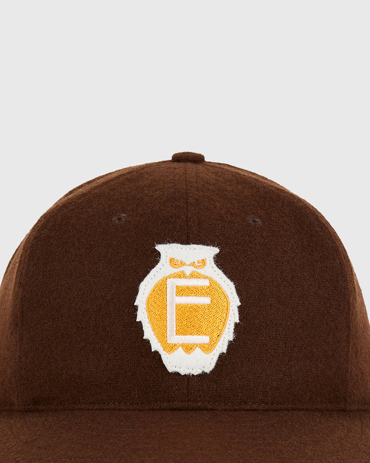 The Tecolotes 1935 Authentic Wool Ballcap by Ebbets Field features a brown crown with a yellow and white owl-shaped patch—containing a stylized letter 