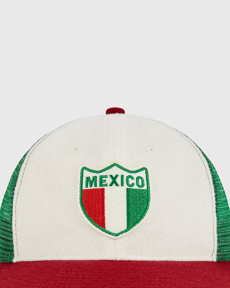 The Ebbets Field Mexico Wool Mesh Trucker Ballcap features a white crown with green mesh side panels and a bold red brim. The front is adorned with a shield patch displaying 