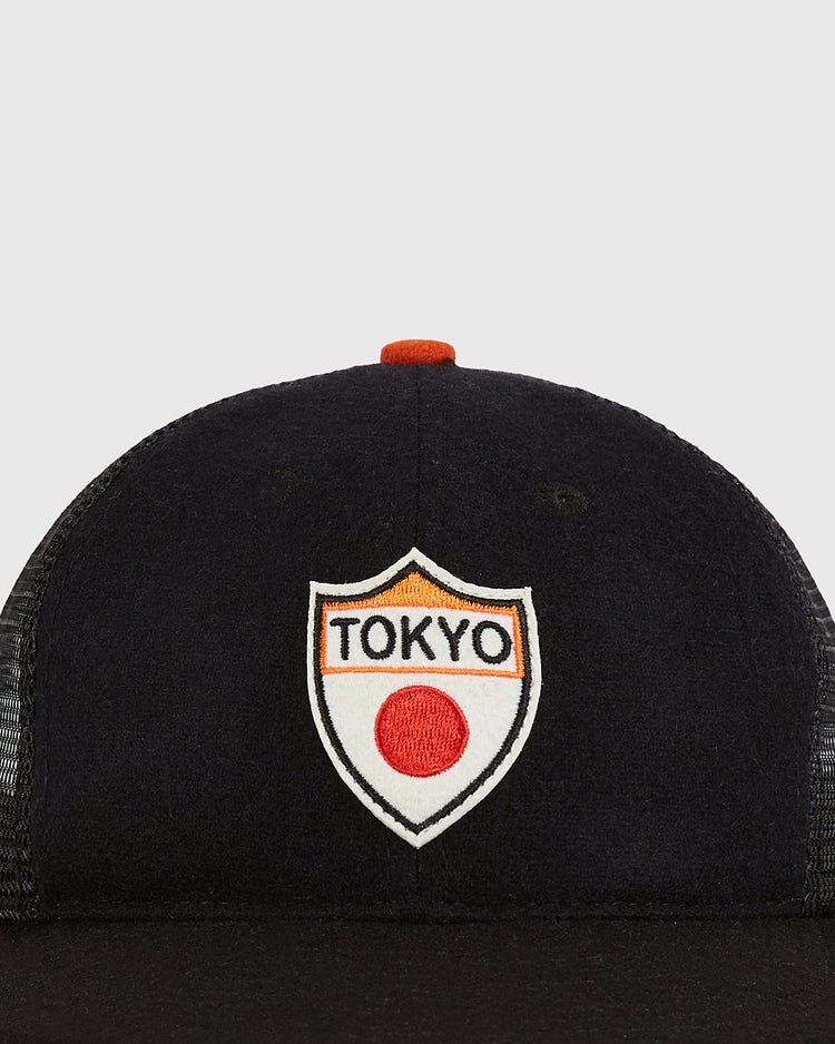 The Ebbets Field Tokyo Giants Wool Mesh Trucker Ballcap is a black vintage-style cap with a mesh back, featuring a shield-shaped patch on the front that displays 
