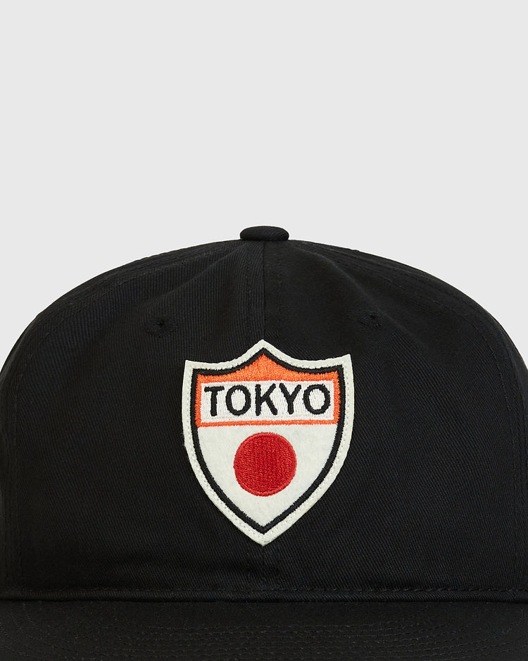 The Ebbets Field Tokyo Giants Patch Cotton Twill Ballcap is a black cap featuring a white shield-shaped patch with “TOKYO” in black letters and a red circle below the text, symbolizing the Japanese flag.