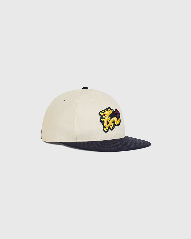 The Ebbets Field Chunichi Dragons Cotton Twill Ballcap features a cream-colored cotton twill crown, a navy brim, and an embroidered yellow dragon patch on the front, inspired by the iconic Chunichi Dragons ballcap. It is displayed on a plain white background.