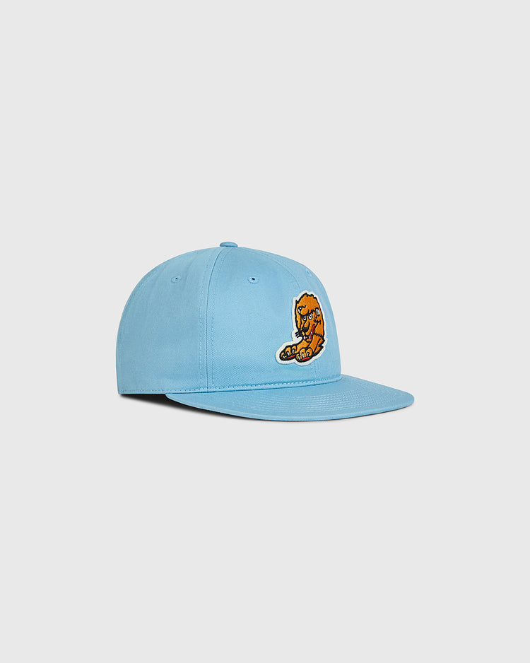 The Ebbets Field Nishitetsu Lions 1971 Cotton Twill Ballcap is crafted from light blue cotton twill and features a flat brim. An embroidered patch of an orange cartoon cat eating pizza decorates the front, adding a playful touch. The ballcap is shown on a plain white background, angled slightly to the left.
