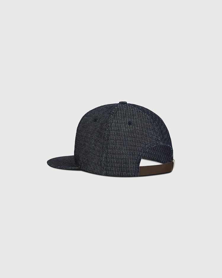 The Ebbets Field Hiroshima Carp Japanese Indigo Cotton Dobby Ballcap is pictured from the back, displaying its brown adjustable strap and flat brim. Crafted from premium Japanese cotton with a textured indigo-dyed finish, the cap is set against a plain light gray background.