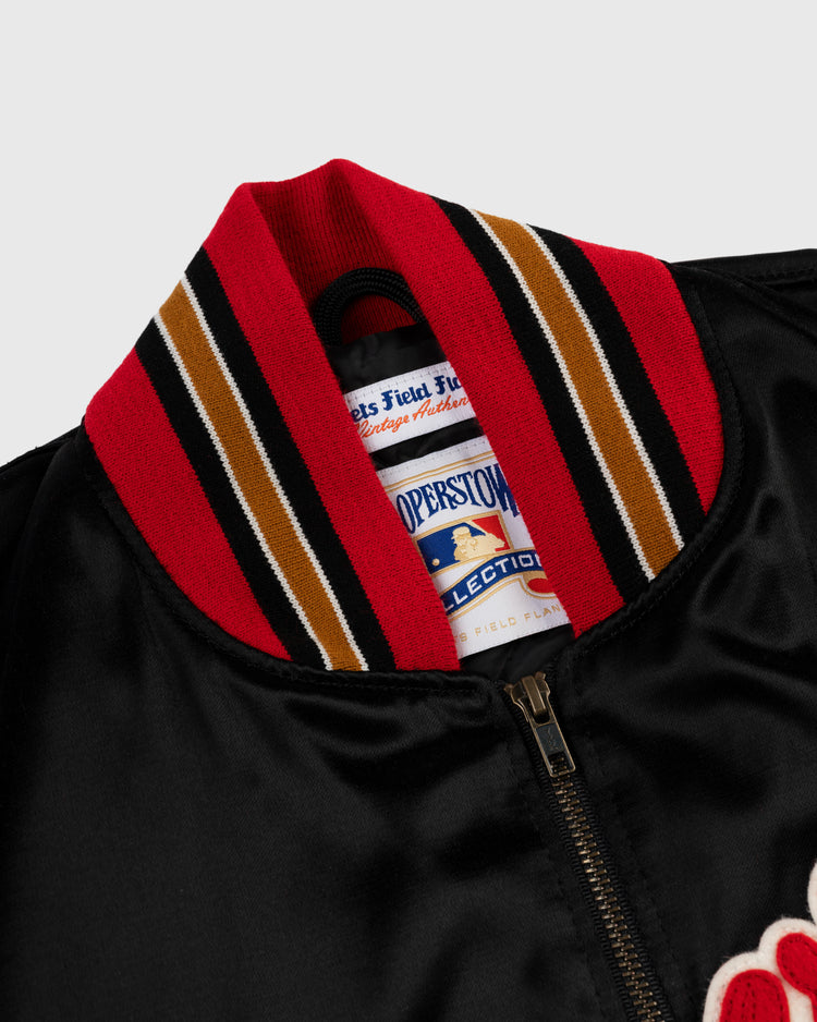 Close-up of an EFF Milwaukee Braves 1957 Authentic All Satin Varsity Jacket in black, featuring a red, black, gold, and white striped ribbed collar. Cooperstown Collection tag inside; metal zipper partially visible at the bottom.