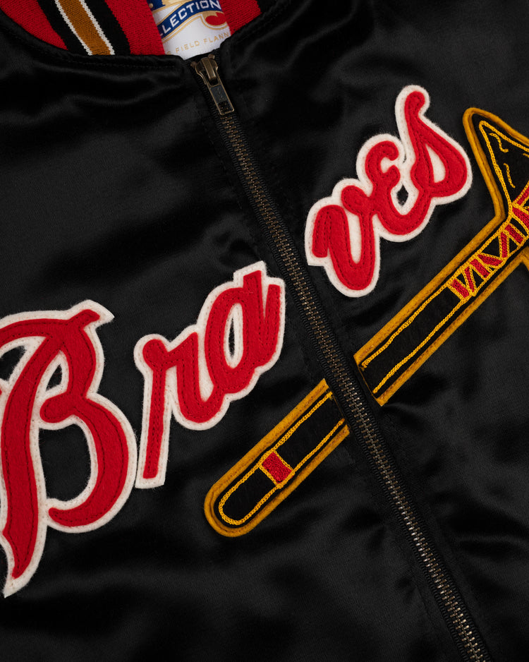 Close-up of the EFF Milwaukee Braves 1957 Authentic All Satin Varsity Jacket in black, featuring red and white Braves lettering, a yellow tomahawk on the front, and a blue and white label inside the collar.