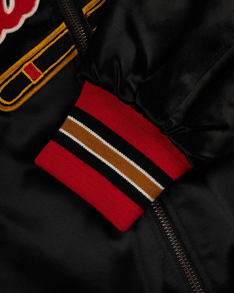 Close-up of the EFF Milwaukee Braves 1957 Authentic All Satin Varsity Jacket, featuring black satin fabric, a red, white, brown, and black striped ribbed cuff, yellow and red embroidery by the zipper.