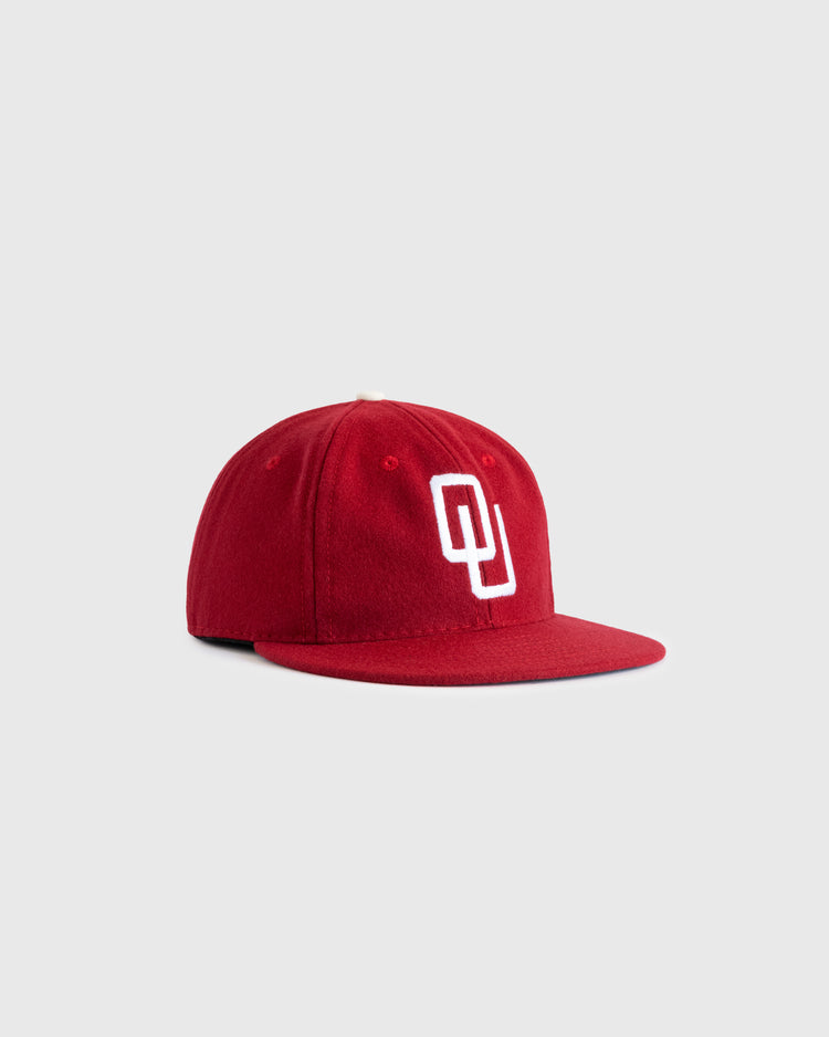 The EFF University of Oklahoma 1975 Authentic Wool Ballcap features a red flat brim and white interlocking OU logo, photographed on a light gray background—ideal for honoring the Sooners’ College World Series heritage.