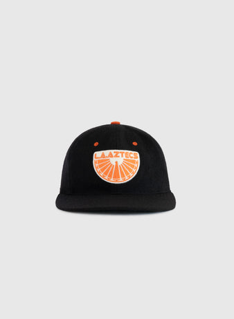 The EFF Los Angeles Aztecs 1976 Authentic Wool Ballcap is a black cap with an orange button and an orange and white LA Aztecs logo featuring a soccer ball, honoring NASL soccer history, shown on a plain light gray background.