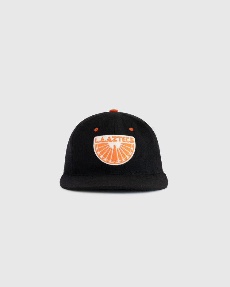 The EFF Los Angeles Aztecs 1976 Authentic Wool Ballcap is a black cap with an orange button and an orange and white LA Aztecs logo featuring a soccer ball, honoring NASL soccer history, shown on a plain light gray background.
