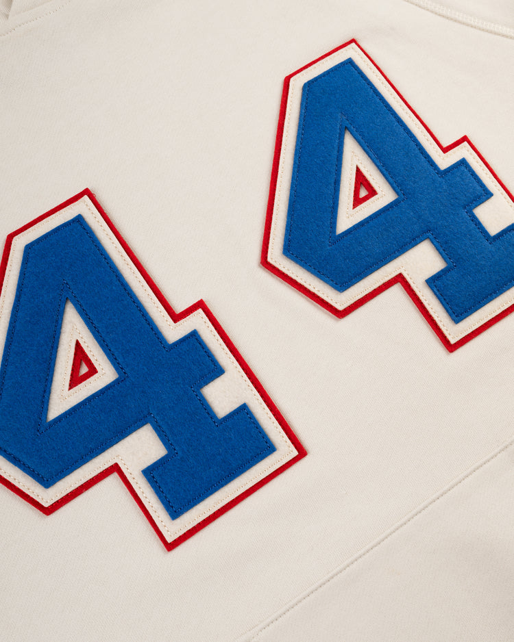 Close-up of two large blue number 4s outlined in white and red, sewn onto off-white fabric on the EFF Hank Aaron French Terry Script Hooded Sweatshirt—evoking memories of Aarons time with the Milwaukee Braves.