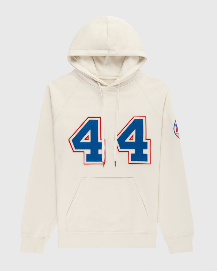 The EFF Hank Aaron French Terry Script Hooded Sweatshirt features a cream color, large blue and red number 44 honoring Hank Aaron of the Milwaukee Braves, a circular patch on the left sleeve, front pocket, and drawstring hood.