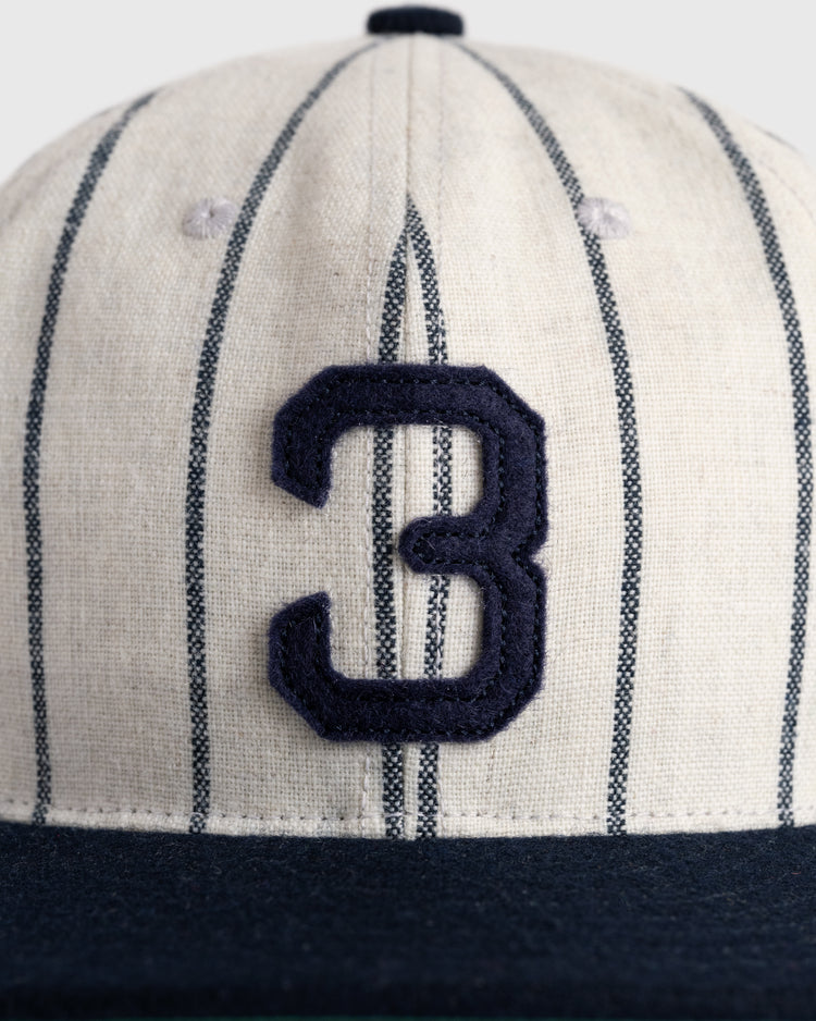 A close-up of the Ebbets Field Flannels Babe Ruth 1932 Signature Series Wool Ballcap, featuring vertical navy pinstripes on cream, a solid navy brim, and a large navy number 3 on the front—a tribute to classic baseball memorabilia.