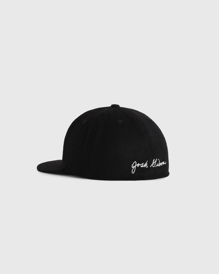 A black Josh Gibson 1945 Signature Series Wool Ballcap by Ebbets Field Flannels is shown from the back left, featuring white cursive Josh Gibson embroidery above the adjustable strap, inspired by vintage Negro Leagues ballcaps.