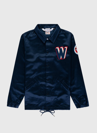 The EFF Washington Senators 1959 Satin Windbreaker Jacket is navy blue with two front pockets, a red and white “W” patch on the chest, a circular sleeve patch, collar, elastic cuffs, and a drawstring hem.