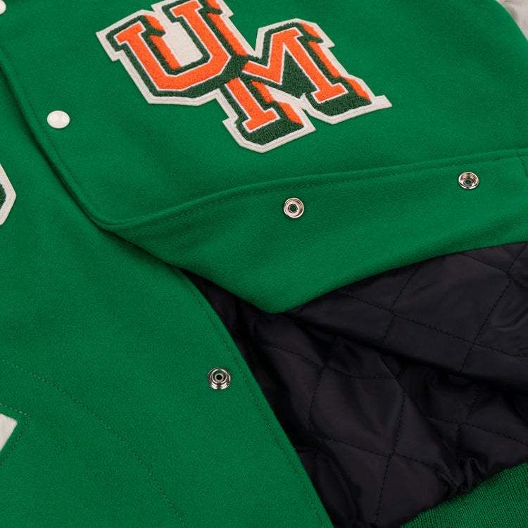 Close-up of the EFF University of Miami 1969 Authentic Jacket, featuring a green exterior, quilted black lining, metal snap buttons, and an orange and white UM chest patch.