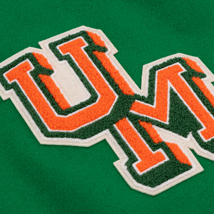 Close-up of orange and green varsity letters U and M with white borders, sewn onto green fabric on the EFF University of Miami 1969 Authentic Jacket, evoking the classic collegiate style.