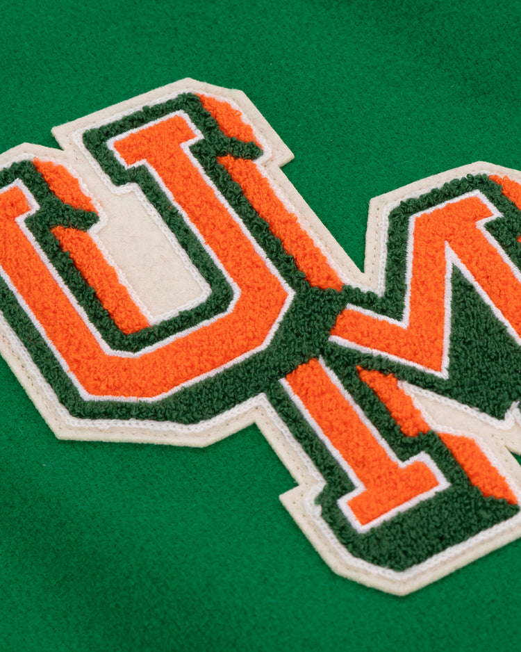 Close-up of orange and green varsity letters U and M with white borders, sewn onto green fabric on the EFF University of Miami 1969 Authentic Jacket, evoking the classic collegiate style.