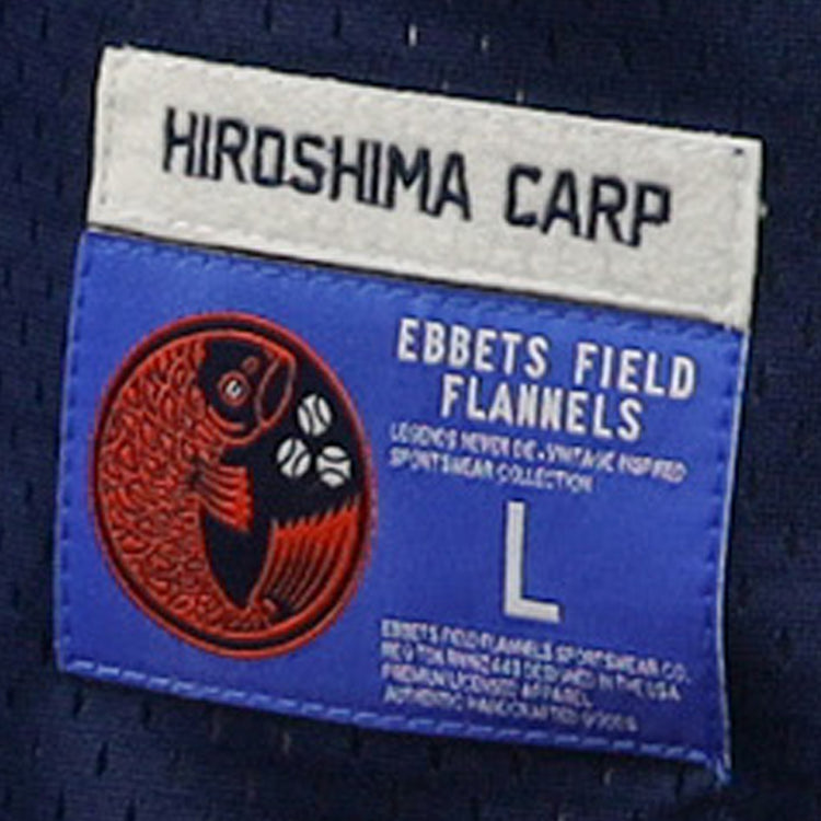 A blue and white label on the EFF Hiroshima Carp DNA Replica V-Neck Mesh Jersey features a red fish logo, size L, and vintage branding—ideal for fans of classic mesh jerseys.