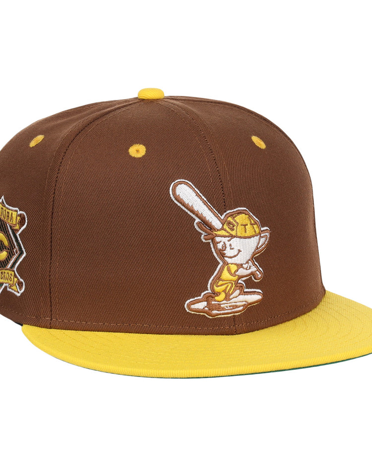 The EFF Cordoba Cafeteros DNA Fitted Ballcap is a vintage-inspired brown cap with a yellow brim, featuring a cartoon baseball character on the front and a yellow-brown side patch, echoing classic Ebbets Field Flannels style.