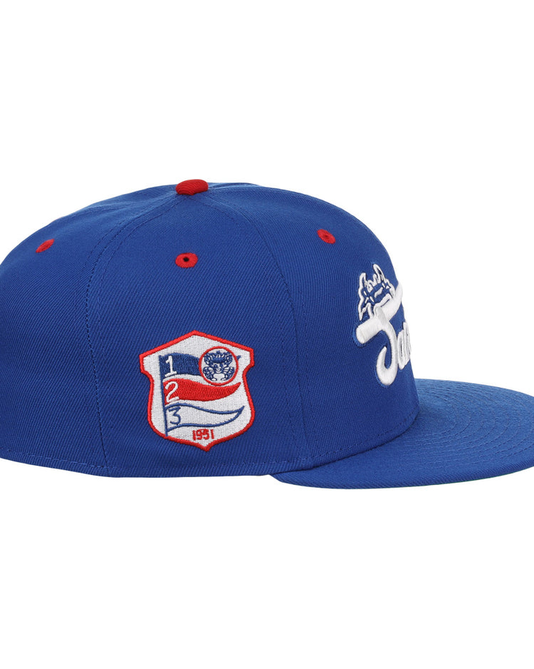 The EFF Santurce Cangrejeros NLB Team Color Fitted Ballcap is a blue vintage-style cap with a flat brim, side white embroidered logo, and a red, white & blue Puerto Rican League patch featuring numbers and shield on the front side panel.