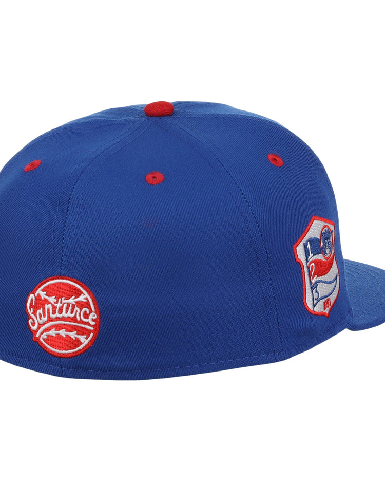 The EFF Santurce Cangrejeros NLB Team Color Fitted Ballcap is a vintage-inspired blue cap with red accents, featuring two embroidered patches: a round red Santurce logo and a shield patch with a flag and number 21 from the Puerto Rican League.